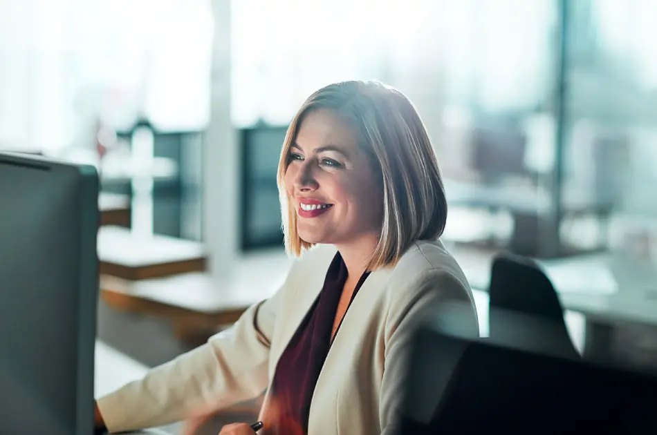 Businesswoman sitting at her desk smiling at computer screen