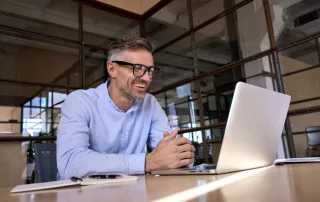 Happy mature business man looking at laptop having virtual meeting in office